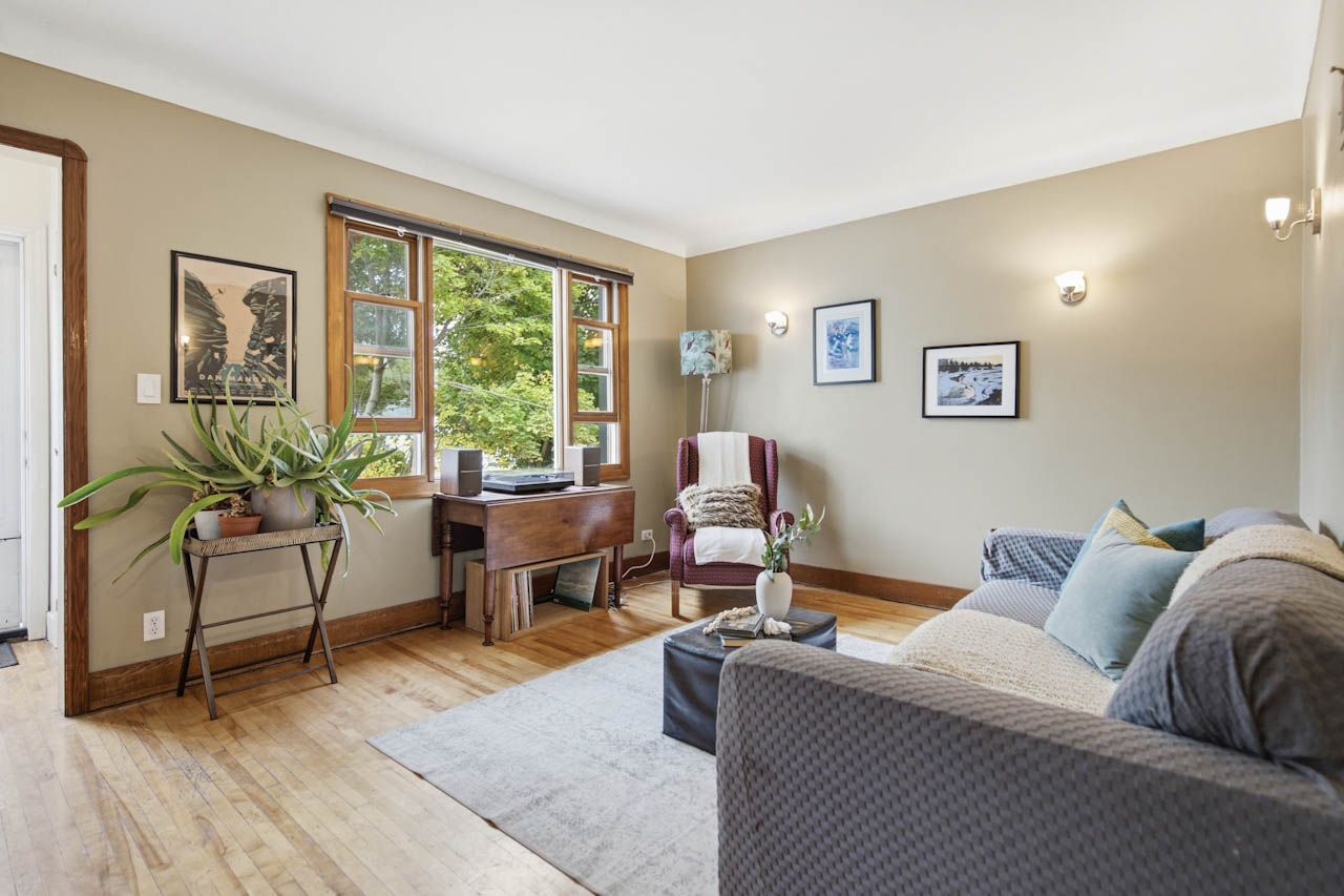 Living room with hardwood floors, wood-trimmed windows, sofa, and reading chair