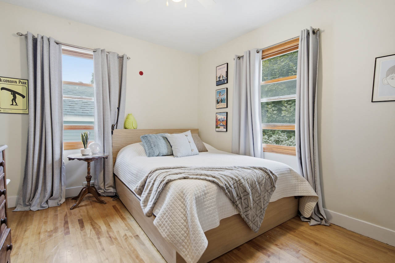 Bedroom with hardwood floor, two windows, and grey curtains