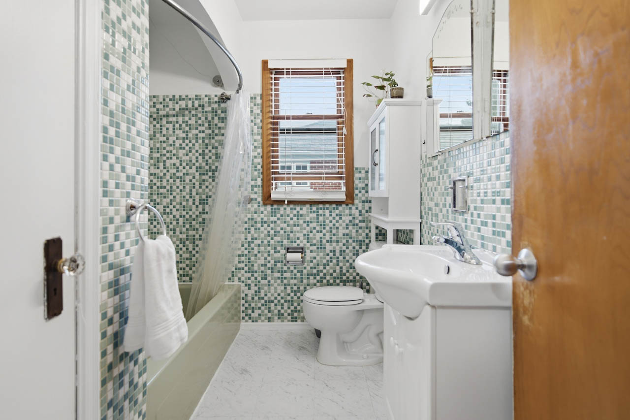 Main bathroom with vintage green mosaic tile, pedestal sink, and window