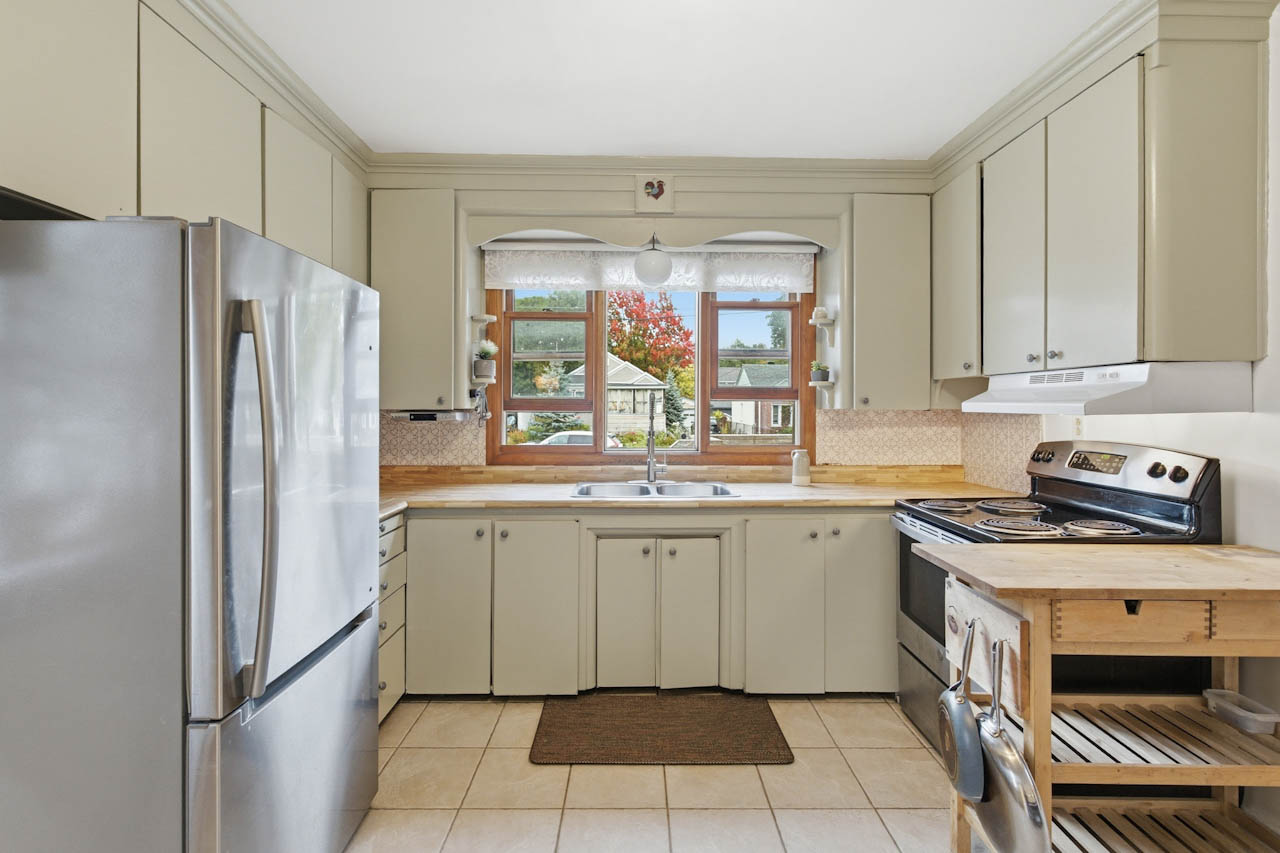 Kitchen with sage cabinets, stainless refrigerator and range, and a window over the sink
